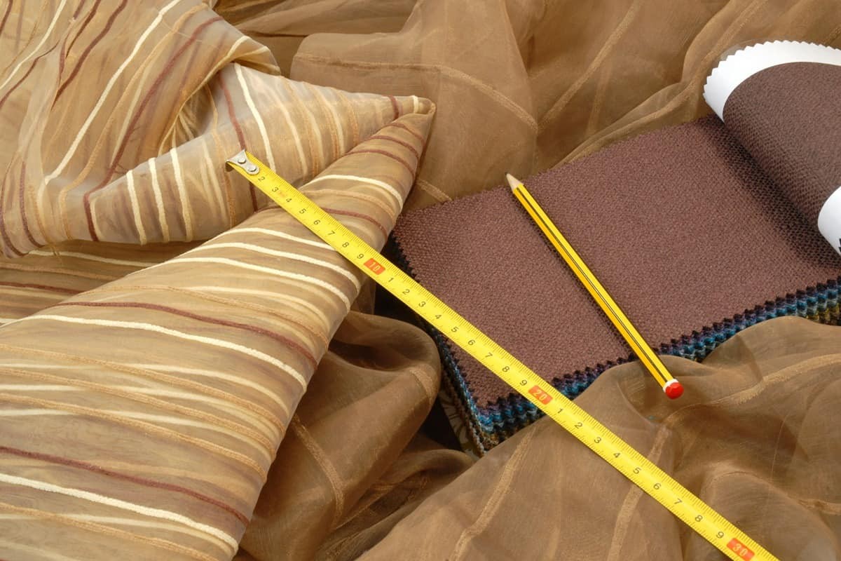 A yellow tape measure and drafting pencil lays across several neurtral curtain fabric samples
