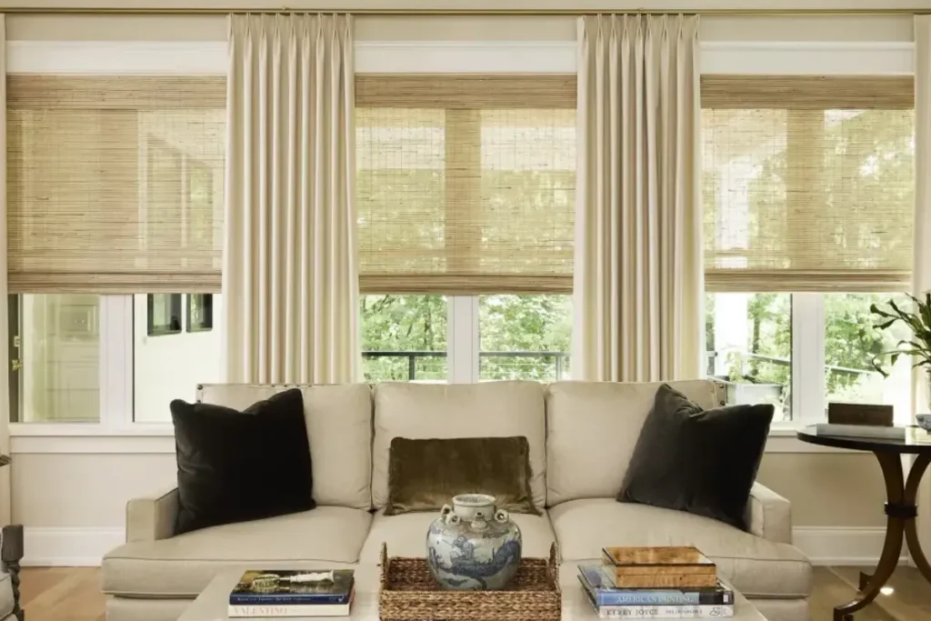 Custom drapery panels on a window with complementing hardware and woven shades in a living room
